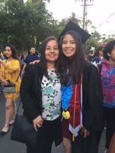 A young woman at college graduation with a smiling mature woman next to her.